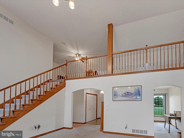 staircase featuring a towering ceiling, carpet, and ceiling fan