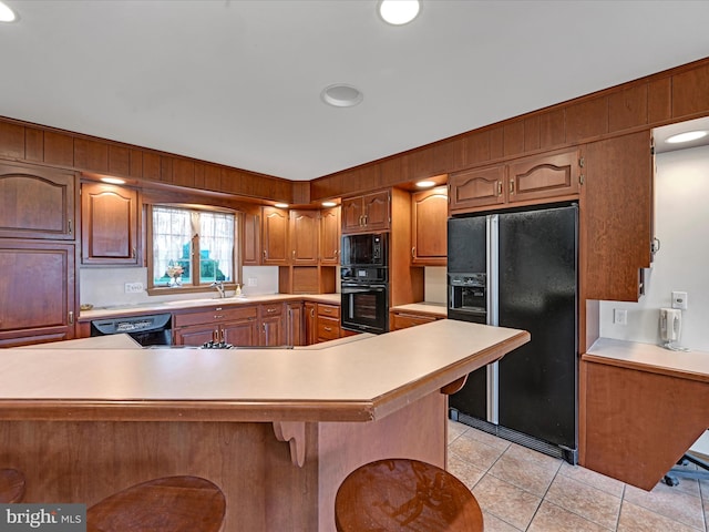 kitchen featuring kitchen peninsula, a kitchen bar, black appliances, sink, and light tile floors