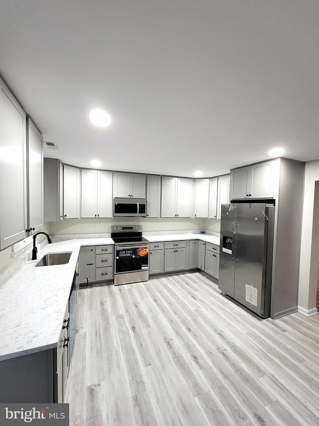 kitchen featuring gray cabinets, stainless steel appliances, light wood-type flooring, and light stone counters