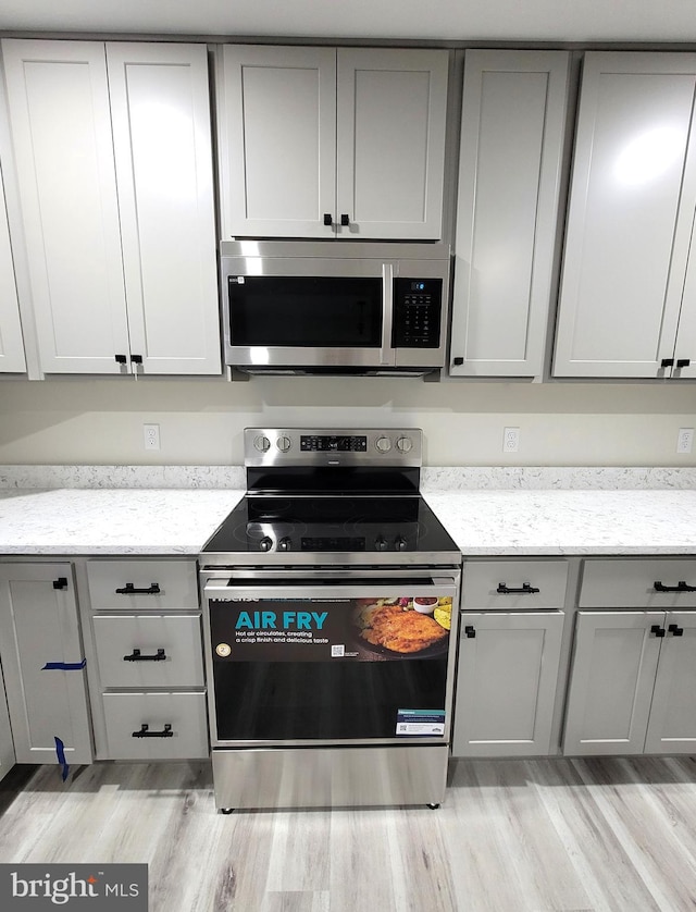 kitchen with appliances with stainless steel finishes, light hardwood / wood-style flooring, light stone counters, and gray cabinets