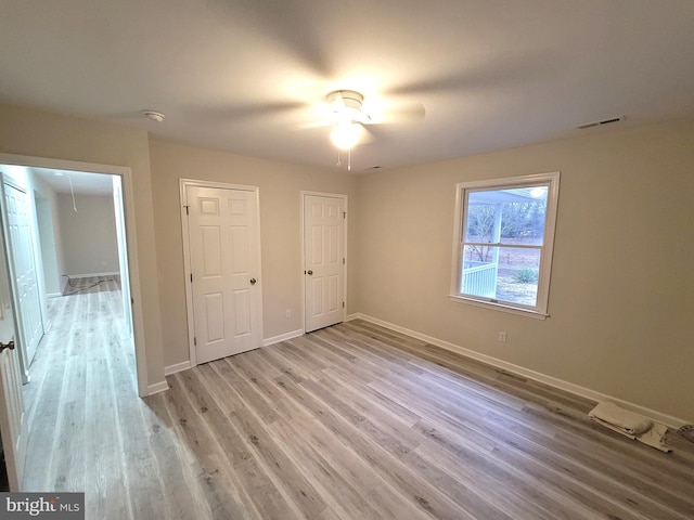 unfurnished bedroom with ceiling fan, multiple closets, and light hardwood / wood-style flooring