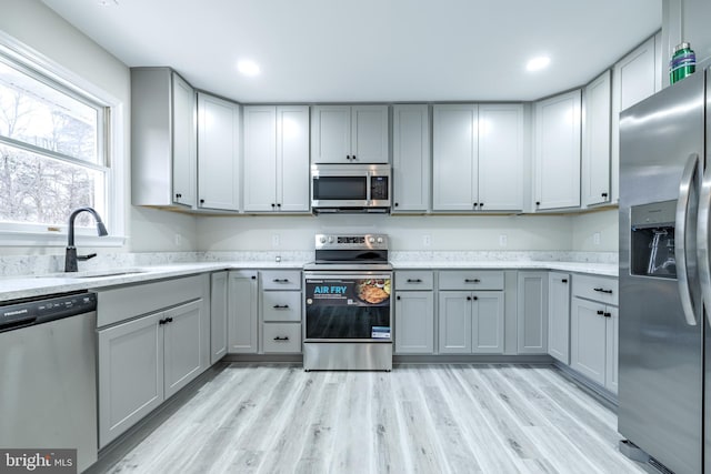 kitchen featuring stainless steel appliances, sink, light stone countertops, gray cabinets, and light hardwood / wood-style floors