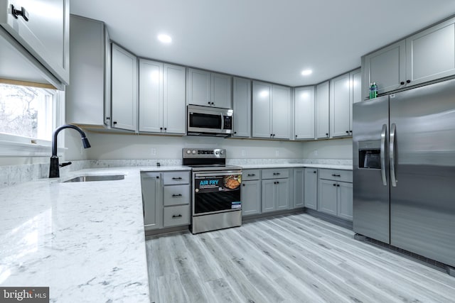 kitchen with appliances with stainless steel finishes, sink, gray cabinets, and light hardwood / wood-style floors