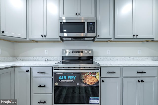 kitchen with light stone countertops, appliances with stainless steel finishes, and gray cabinetry