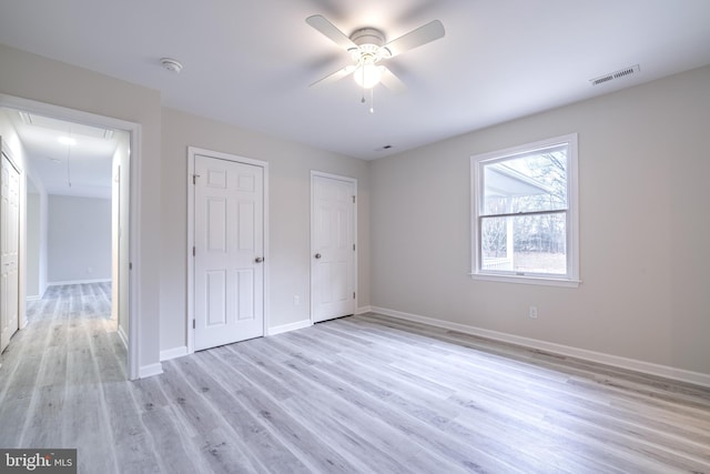 unfurnished bedroom with light hardwood / wood-style floors, multiple closets, and ceiling fan