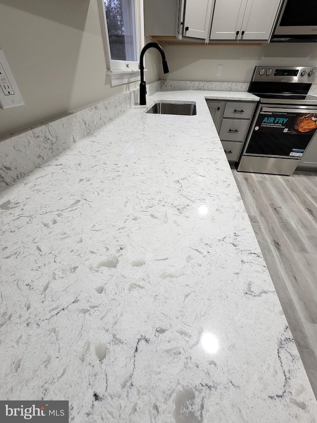 interior details featuring stainless steel range with electric cooktop, light stone countertops, gray cabinets, sink, and light hardwood / wood-style floors