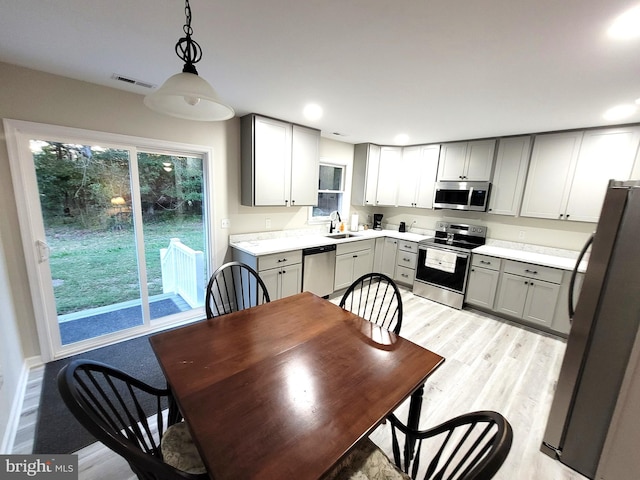 kitchen with hanging light fixtures, light hardwood / wood-style flooring, sink, gray cabinetry, and stainless steel appliances