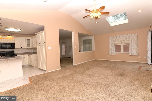 unfurnished living room with ceiling fan, vaulted ceiling with skylight, and light tile patterned floors