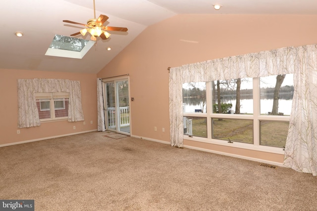 unfurnished living room with a skylight, ceiling fan, a water view, high vaulted ceiling, and carpet floors