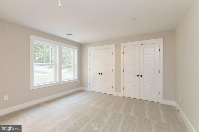 unfurnished bedroom with light colored carpet and two closets