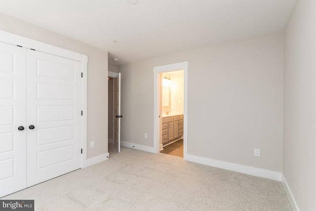 unfurnished bedroom with ensuite bathroom, a closet, and light colored carpet