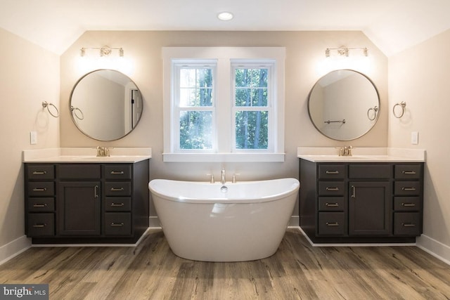 bathroom featuring hardwood / wood-style floors, vanity, vaulted ceiling, and a bathing tub