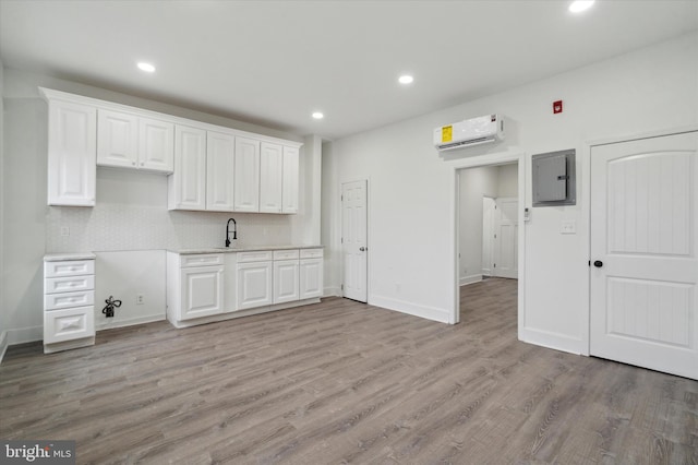 kitchen featuring white cabinets, tasteful backsplash, light hardwood / wood-style floors, and a wall mounted air conditioner