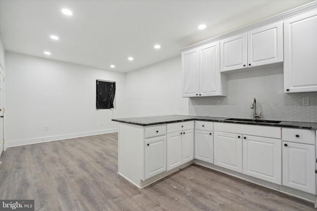 kitchen featuring kitchen peninsula, white cabinets, backsplash, light wood-type flooring, and sink