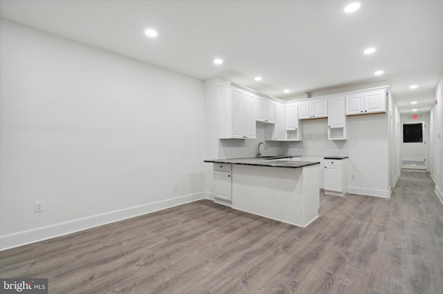 kitchen with kitchen peninsula, sink, light wood-type flooring, white cabinets, and tasteful backsplash