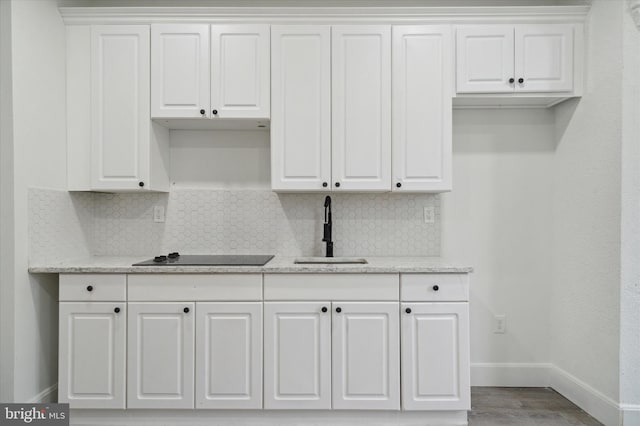 kitchen featuring backsplash, black electric cooktop, sink, white cabinets, and hardwood / wood-style flooring