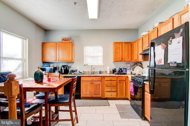 kitchen featuring a textured ceiling, sink, light tile floors, and black appliances