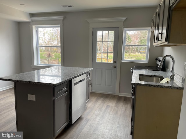 kitchen featuring light wood-type flooring, stainless steel dishwasher, sink, stone countertops, and a kitchen island