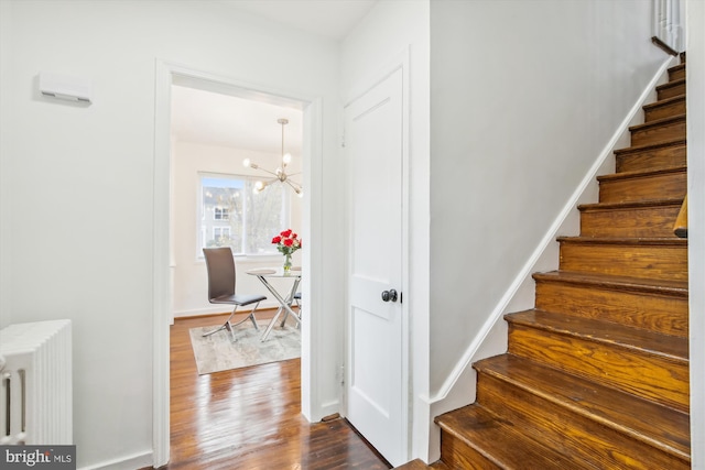 stairs featuring dark hardwood / wood-style floors, a notable chandelier, and radiator heating unit