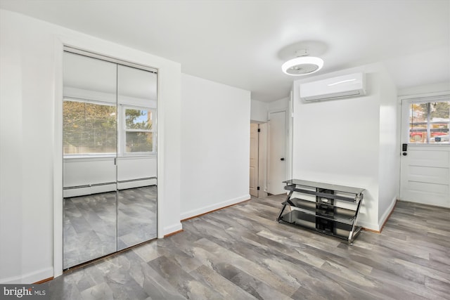 interior space featuring baseboard heating, a wealth of natural light, hardwood / wood-style flooring, and a wall unit AC