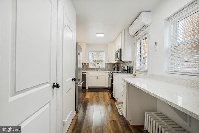 kitchen with a wall mounted AC, dark hardwood / wood-style flooring, white cabinets, stainless steel appliances, and light stone countertops