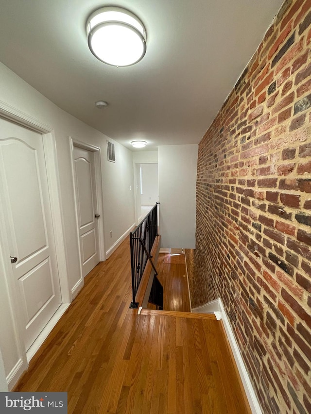 corridor with dark wood-type flooring and brick wall