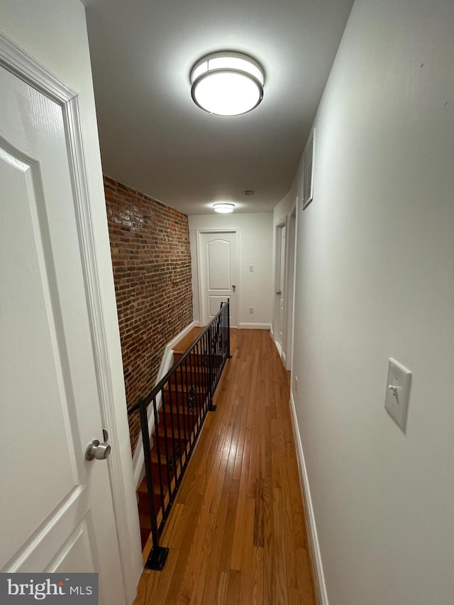 corridor with brick wall and hardwood / wood-style floors