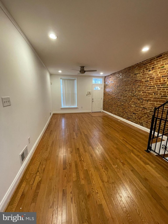 empty room with brick wall, dark wood-type flooring, ornamental molding, and ceiling fan