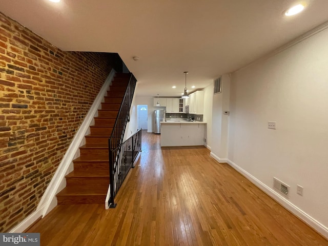 stairway featuring light hardwood / wood-style flooring, crown molding, and brick wall