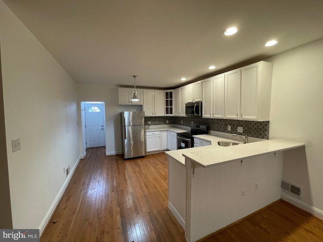 kitchen featuring stainless steel appliances, kitchen peninsula, hardwood / wood-style floors, and white cabinets