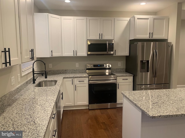 kitchen featuring dark wood-type flooring, appliances with stainless steel finishes, sink, white cabinets, and light stone counters