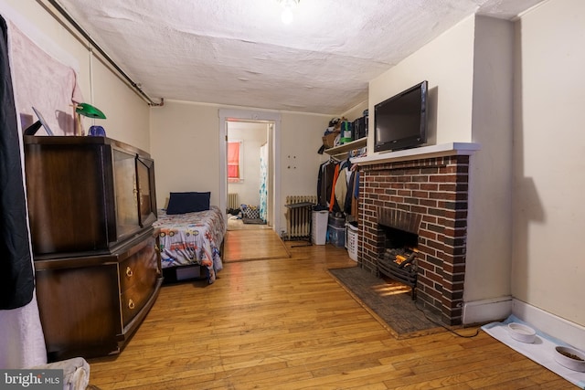 living room with a fireplace, radiator heating unit, a textured ceiling, and light hardwood / wood-style flooring