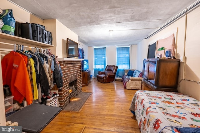 bedroom with light hardwood / wood-style flooring, a textured ceiling, and a brick fireplace