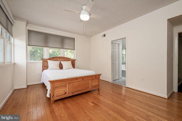 bedroom featuring a textured ceiling, connected bathroom, light hardwood / wood-style flooring, and ceiling fan