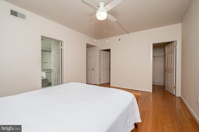 bedroom featuring light wood-type flooring, a walk in closet, a textured ceiling, ceiling fan, and connected bathroom