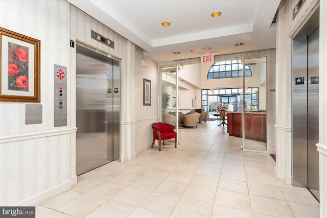 hallway featuring light tile patterned flooring, elevator, and a tray ceiling