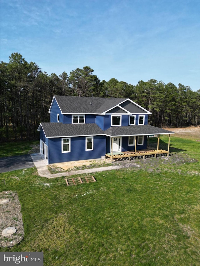 view of front of home featuring a front yard, a porch, a forest view, and aphalt driveway