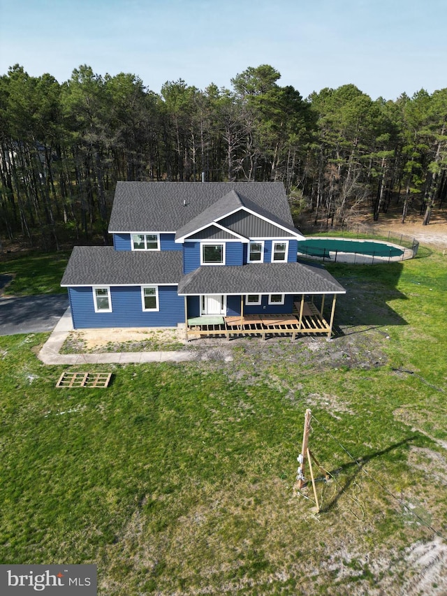 rear view of property featuring a lawn, a wooded view, and a shingled roof