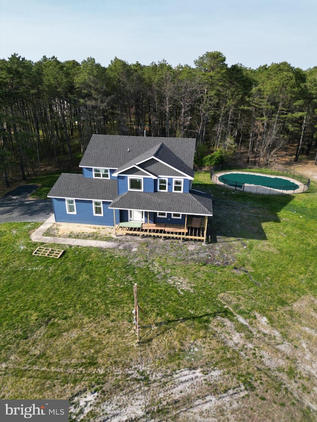 back of house featuring a forest view, a wooden deck, an outdoor pool, and a yard