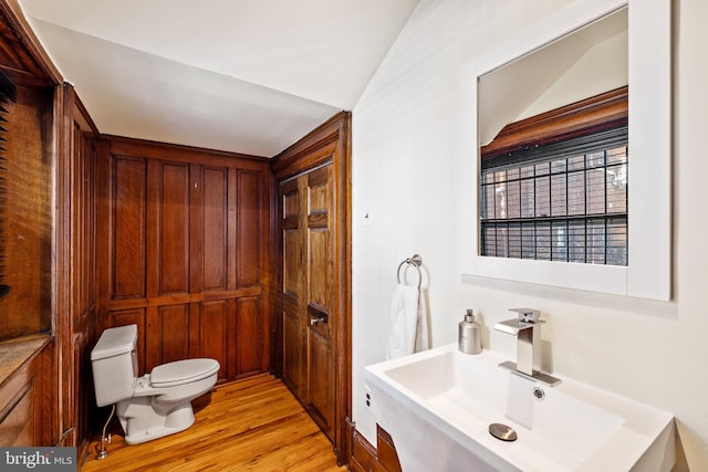 bathroom with wood-type flooring, toilet, lofted ceiling, and sink