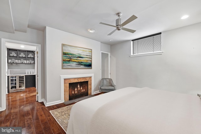 bedroom with a premium fireplace, ceiling fan, dark hardwood / wood-style flooring, and beverage cooler