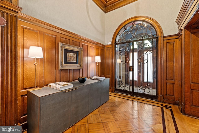 foyer with light parquet flooring, wooden walls, a towering ceiling, and ornamental molding