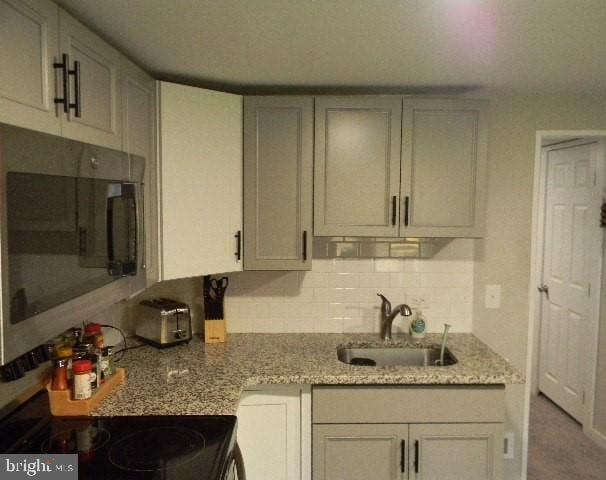 kitchen with backsplash, white cabinets, black range, sink, and light stone countertops