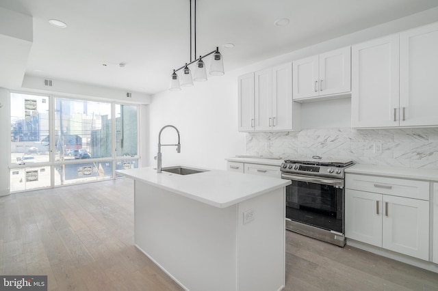 kitchen featuring a kitchen island with sink, sink, stainless steel stove, decorative light fixtures, and white cabinetry