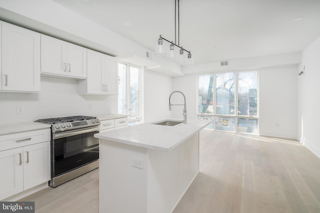 kitchen with sink, stainless steel stove, hanging light fixtures, an island with sink, and white cabinets