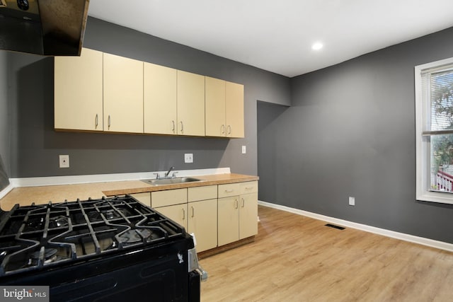 kitchen with black stove, sink, light hardwood / wood-style floors, and cream cabinetry