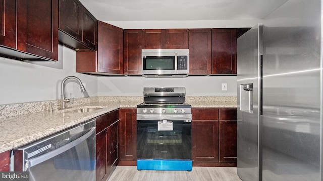 kitchen featuring light stone countertops, sink, light wood-type flooring, and appliances with stainless steel finishes