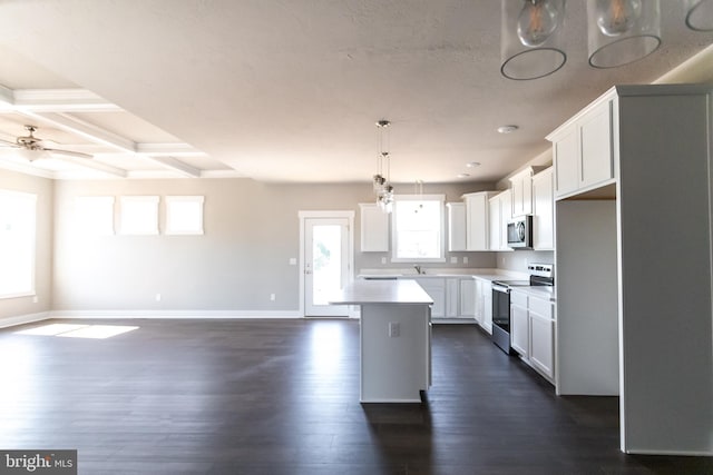 kitchen with appliances with stainless steel finishes, a wealth of natural light, coffered ceiling, white cabinets, and a center island