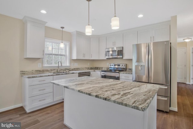 kitchen with appliances with stainless steel finishes, a kitchen island, light wood-type flooring, and white cabinets