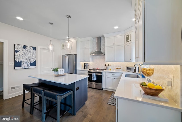 kitchen with dark wood-type flooring, white cabinets, wall chimney exhaust hood, a kitchen island, and stainless steel appliances